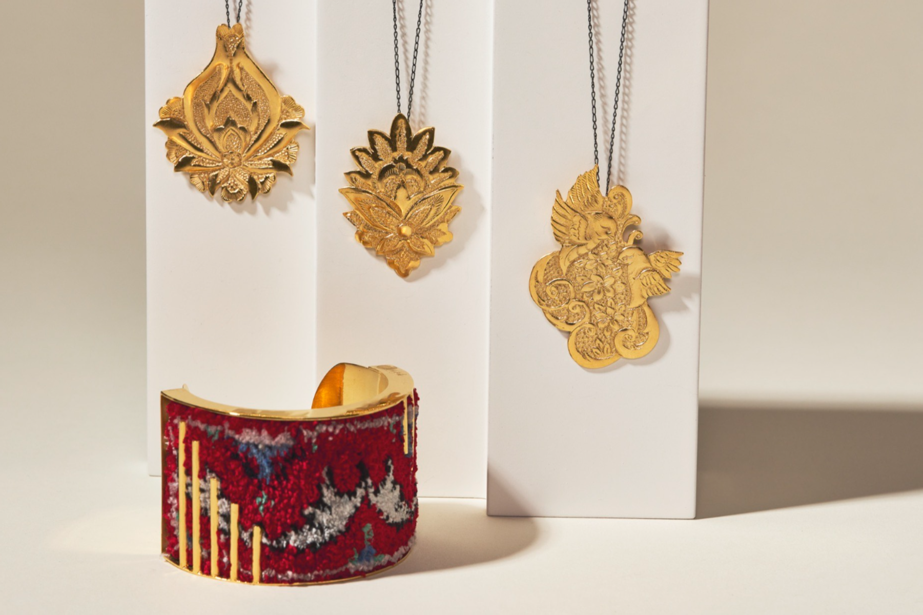Silk Road - A Golden Bangle Woven with silk Persian carpet next to Hand-chased Golden Pendants Inspired by the Enchanting Patterns of Persian Carpets, a Trio of Timeless 